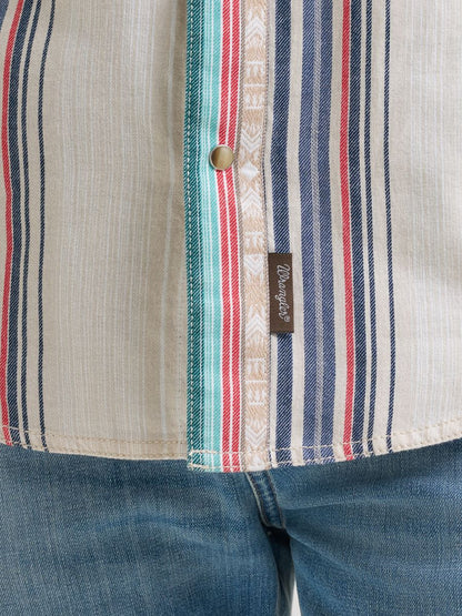 Close-up of a striped shirt with a Wrangler brand label, worn with blue jeans.