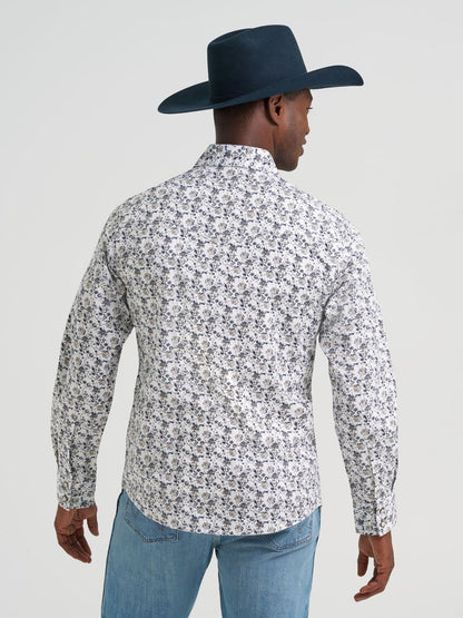 Man wearing a patterned Wrangler floral shirt, blue jeans, and a dark cowboy hat on a light gray background