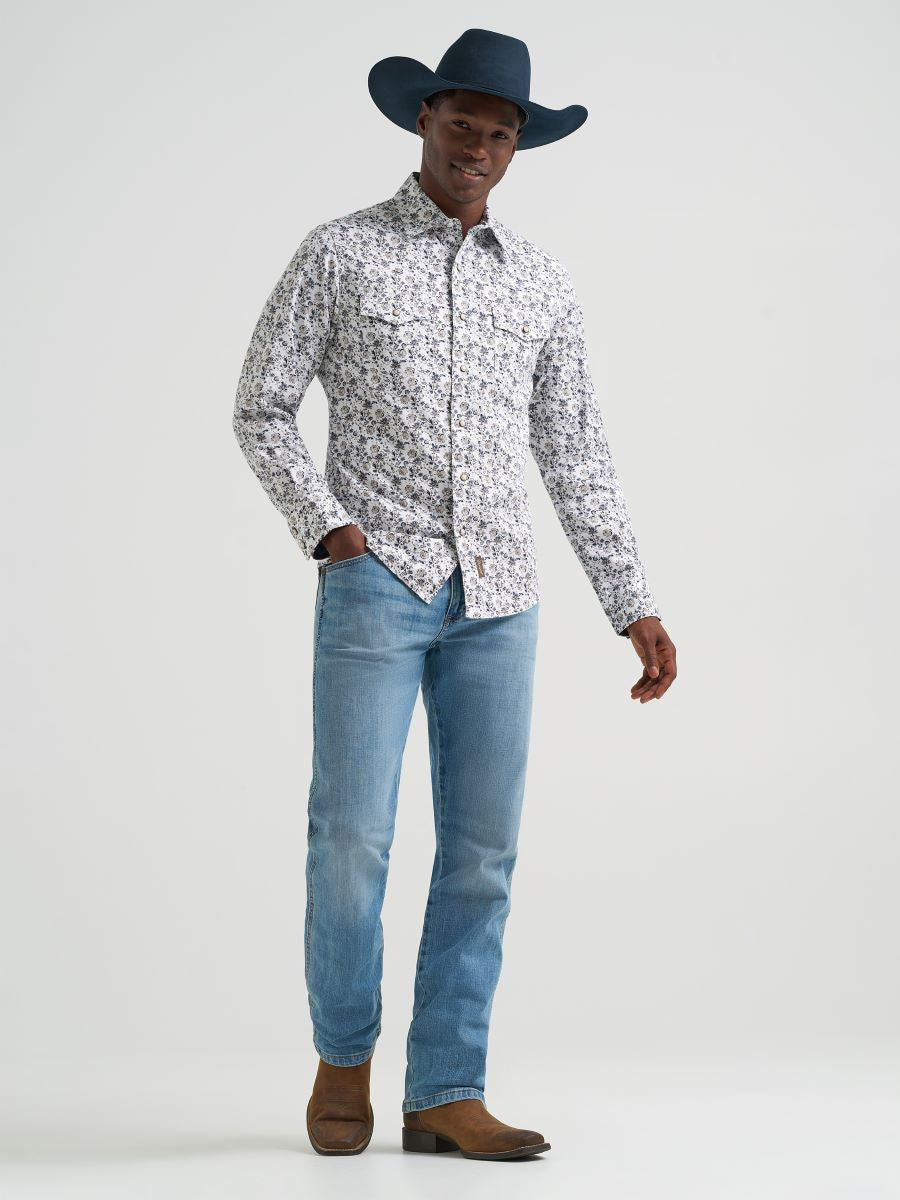 Man wearing a patterned Wrangler shirt, blue jeans, and a dark cowboy hat on a light gray background