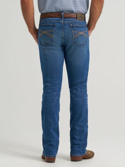 Rear view of a man wearing blue denim Wrangler jeans with brown leather belt and brown shoes, against a light gray studio background.
