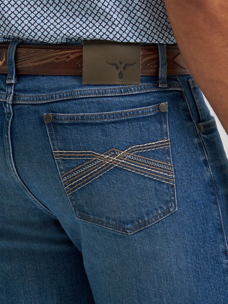 Close-up of the back pocket of blue Wrangler denim jeans with decorative contrast stitching, a brown leather belt, and a dark brown leather patch featuring a longhorn logo.
