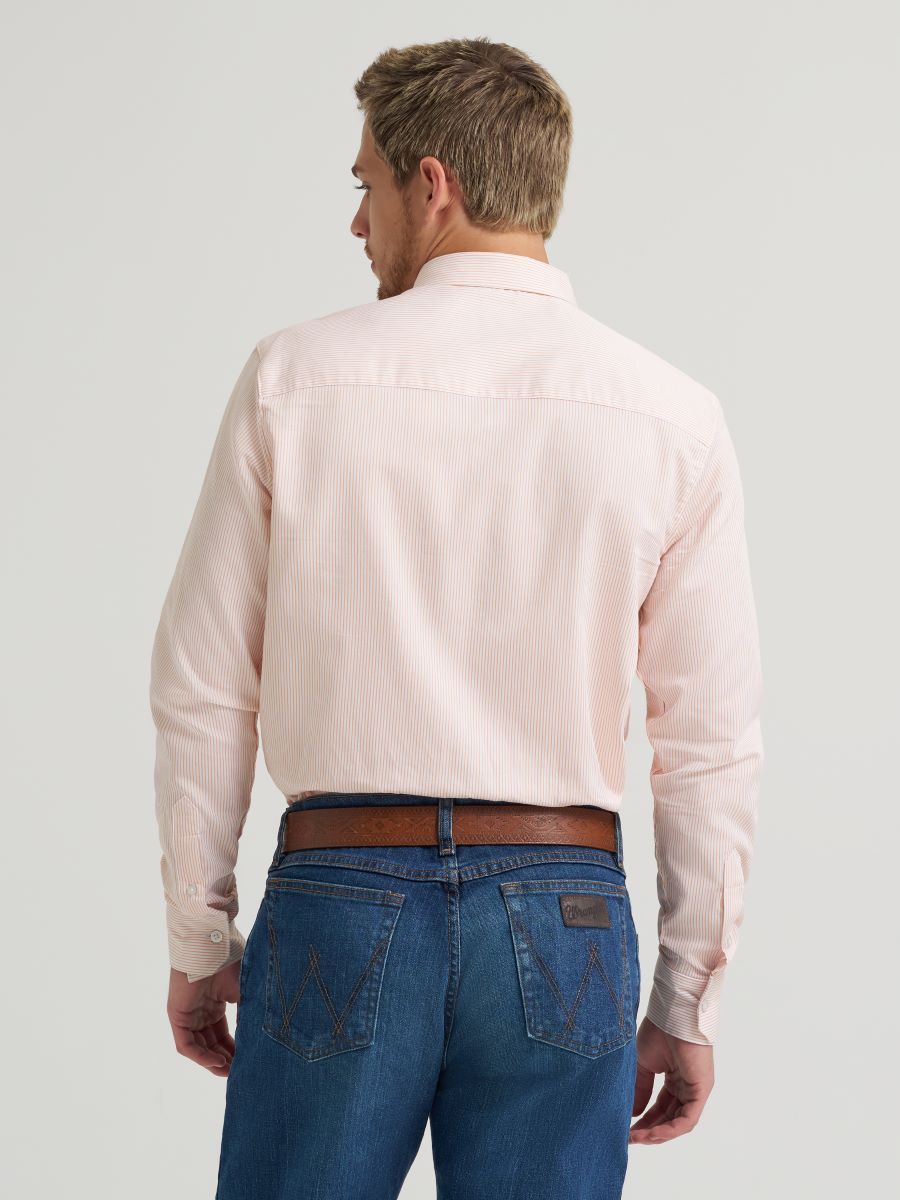 Man wearing a light pink Wrangler shirt and blue jeans on a plain background