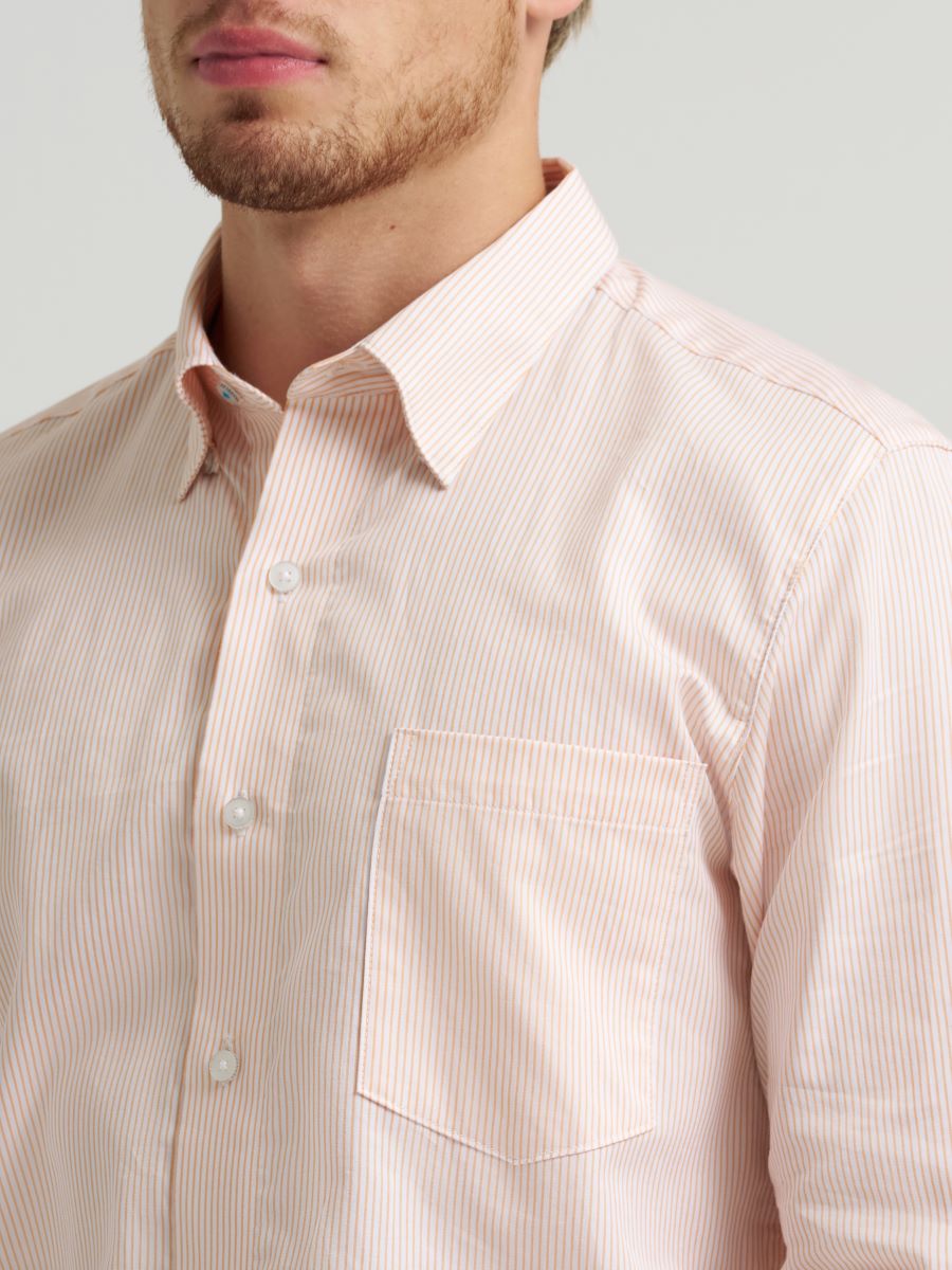 Man wearing a light pink Wrangler shirt on a plain background
