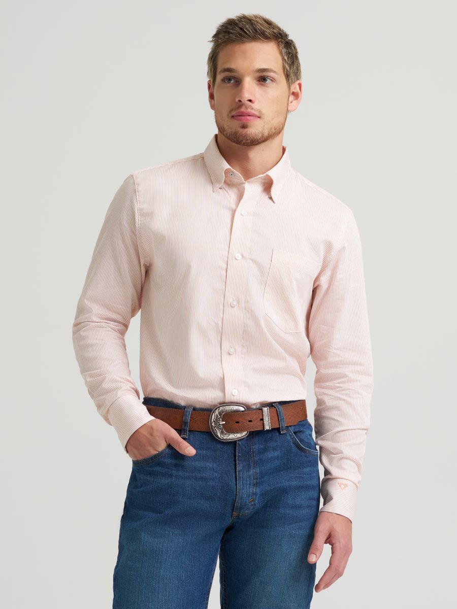 Man wearing a light pink Wrangler shirt and blue jeans on a plain background