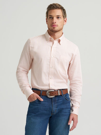 Man wearing a light pink Wrangler shirt and blue jeans on a plain background
