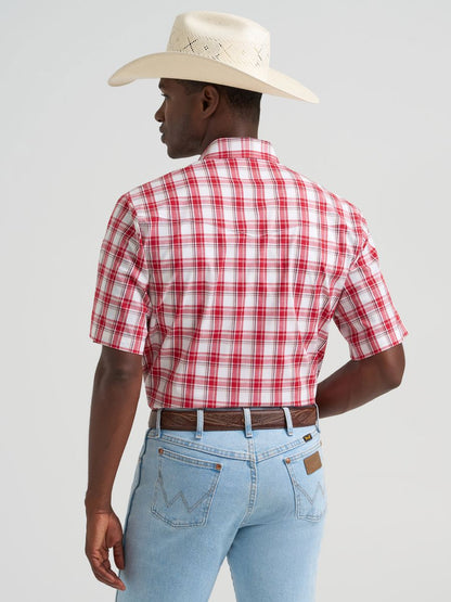 Man wearing a red plaid Wrangler shirt, light blue jeans, and a white cowboy hat on a gray background