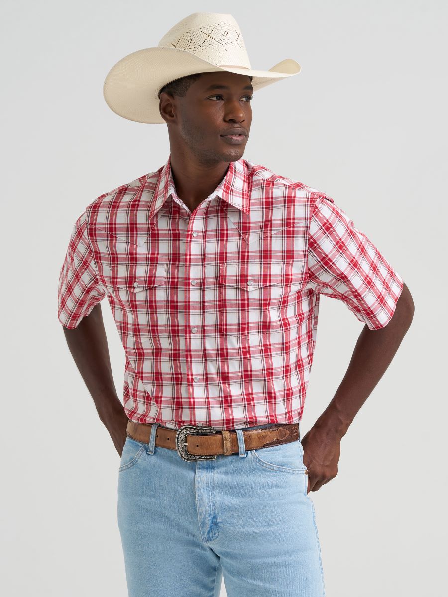 Man wearing a red plaid Wrangler shirt, light blue jeans, and a white cowboy hat on a gray background