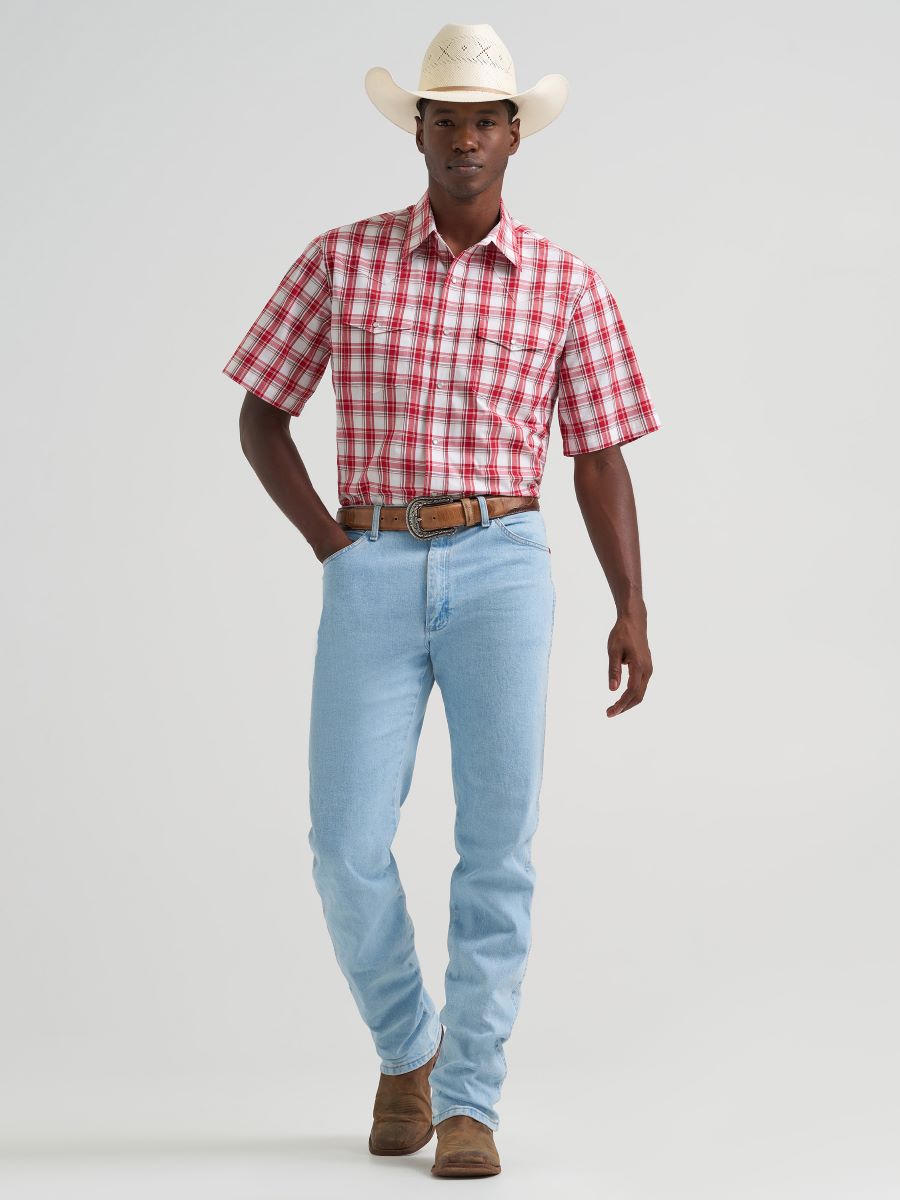 Man wearing a red plaid Wrangler shirt, light blue jeans, and a white cowboy hat on a gray background