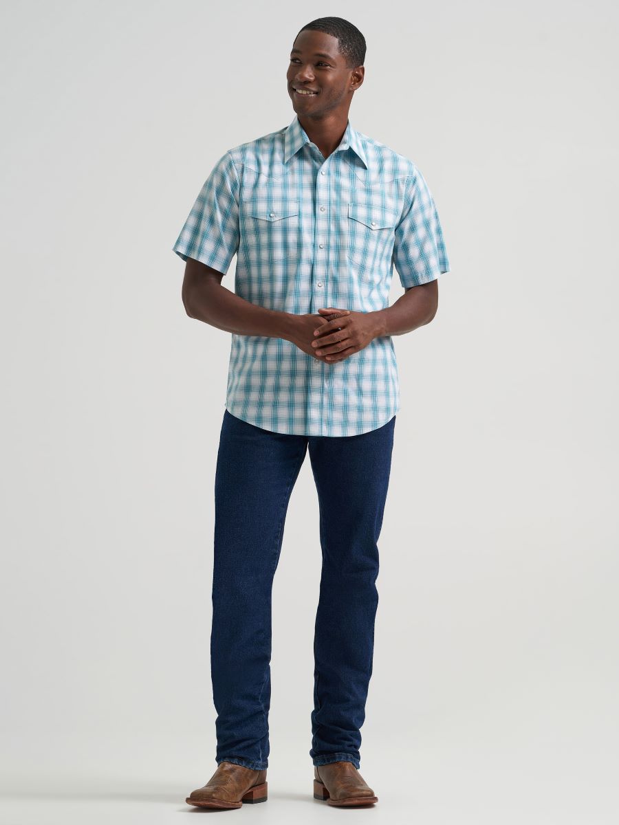 Man wearing a blue and white checkered Wrangler shirt and dark blue jeans on a light gray background