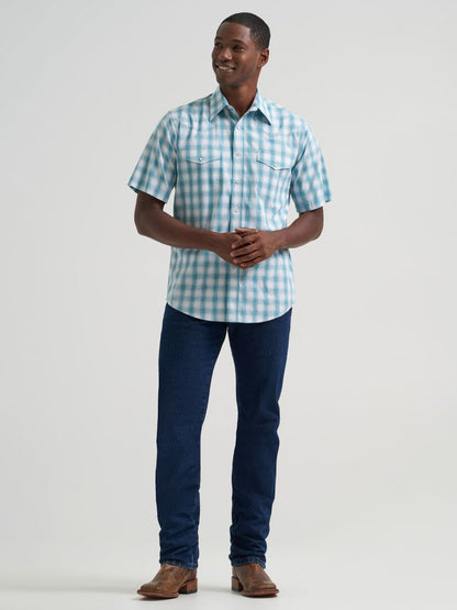 Man wearing a blue and white checkered Wrangler shirt and dark blue jeans on a light gray background