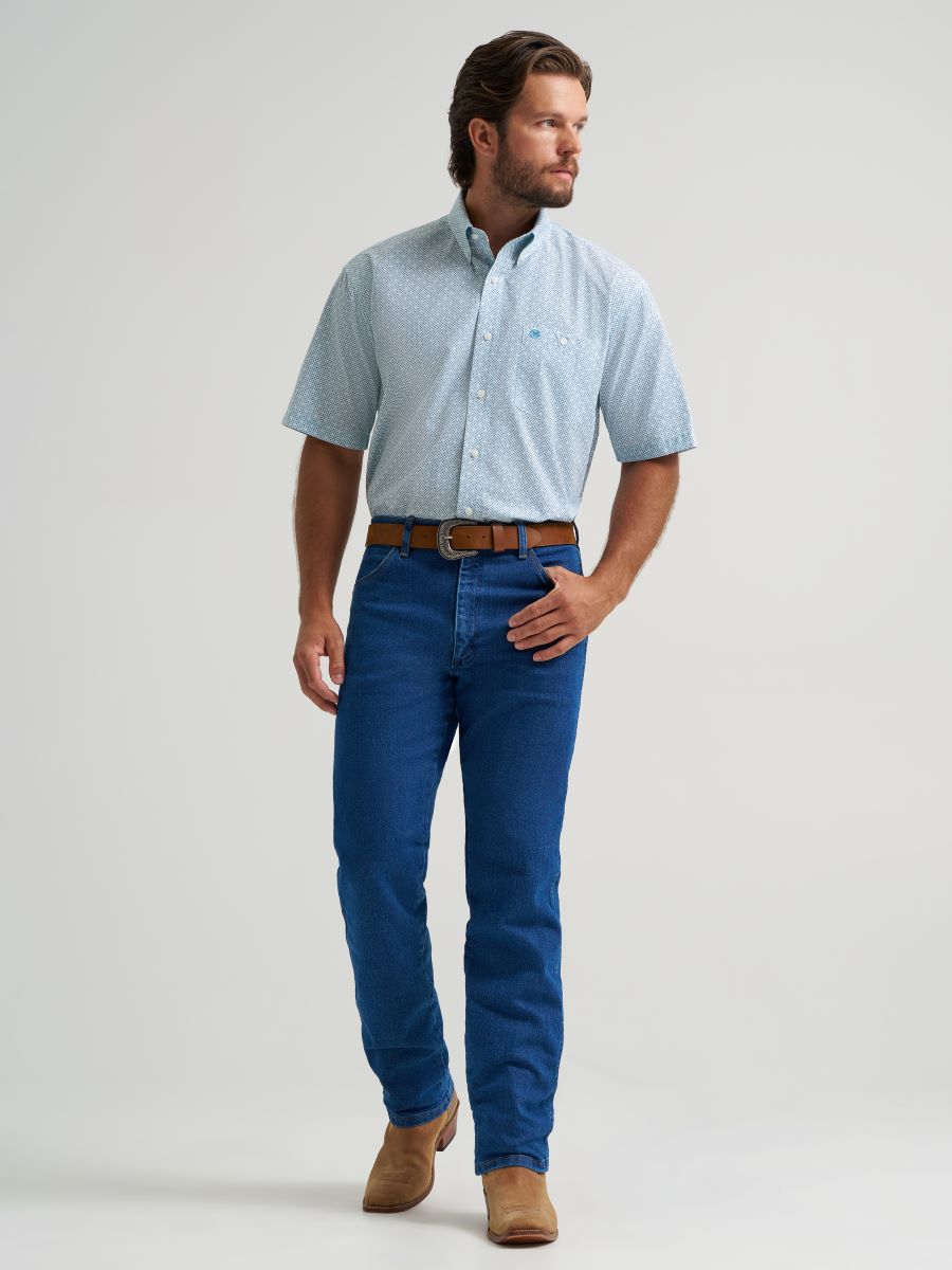 Man wearing a light blue button-up Wrangler shirt and blue jeans on a gray background
