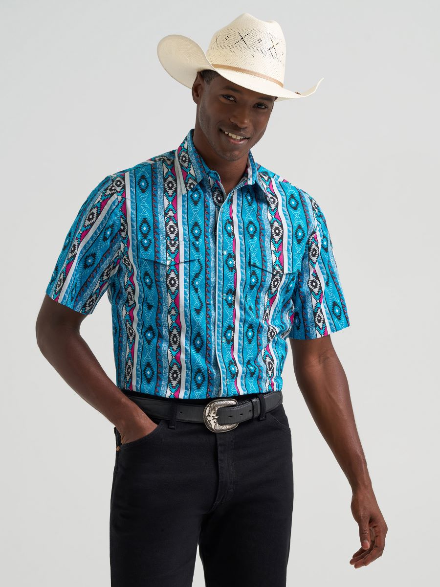 man wearing a Blue Wrangler shirt with hat and blue jeans on a grey background