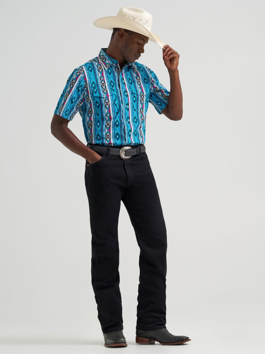 man wearing a Blue Wrangler shirt with hat and blue jeans on a grey background
