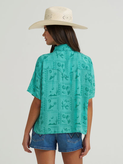 woman wearing a green Wrangler shirt, denim shorts and cowboy hat on a white background