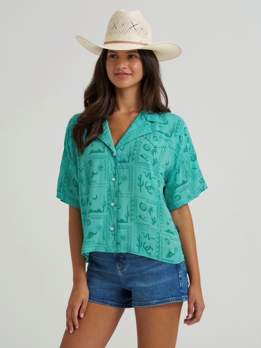 woman wearing a green Wrangler shirt, denim shorts and cowboy hat on a white background
