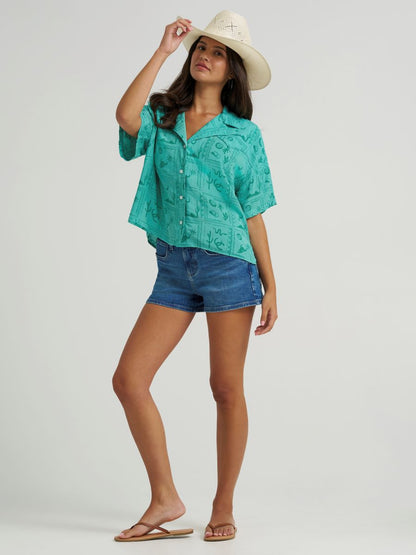 woman wearing a green Wrangler shirt, denim shorts and cowboy hat on a white background