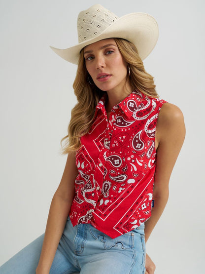Woman wearing a red Wrangler paisley tank top, cowboy hat and blue jeans on a grey background