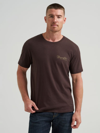 Man wearing a brown Wrangler t-shirt with a logo on a gray background