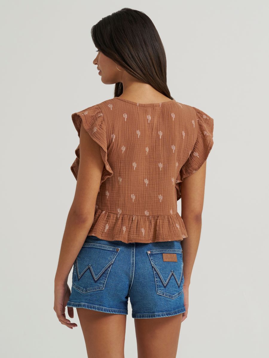 Woman wearing a brown Wrangler ruffled blouse and blue shorts on a white background