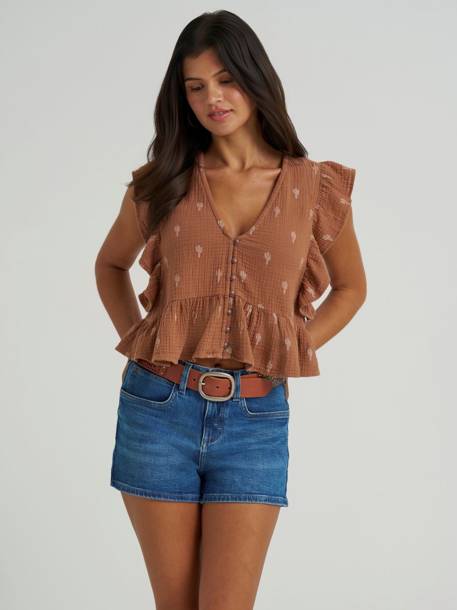 Woman wearing a brown Wrangler ruffled blouse and blue shorts on a white background
