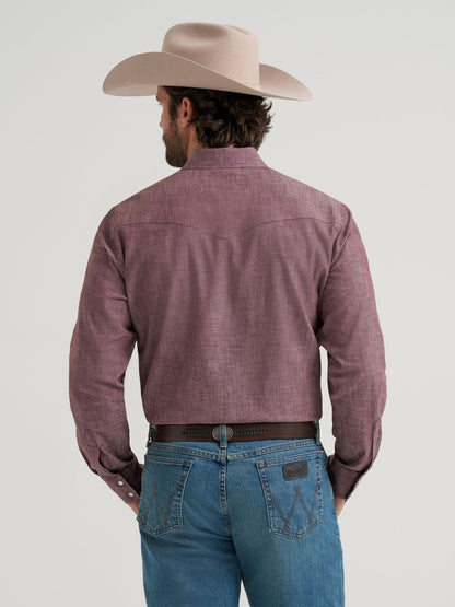 Man wearing a purple button-up Wrangler shirt, blue jeans, and a beige cowboy hat on a light gray background