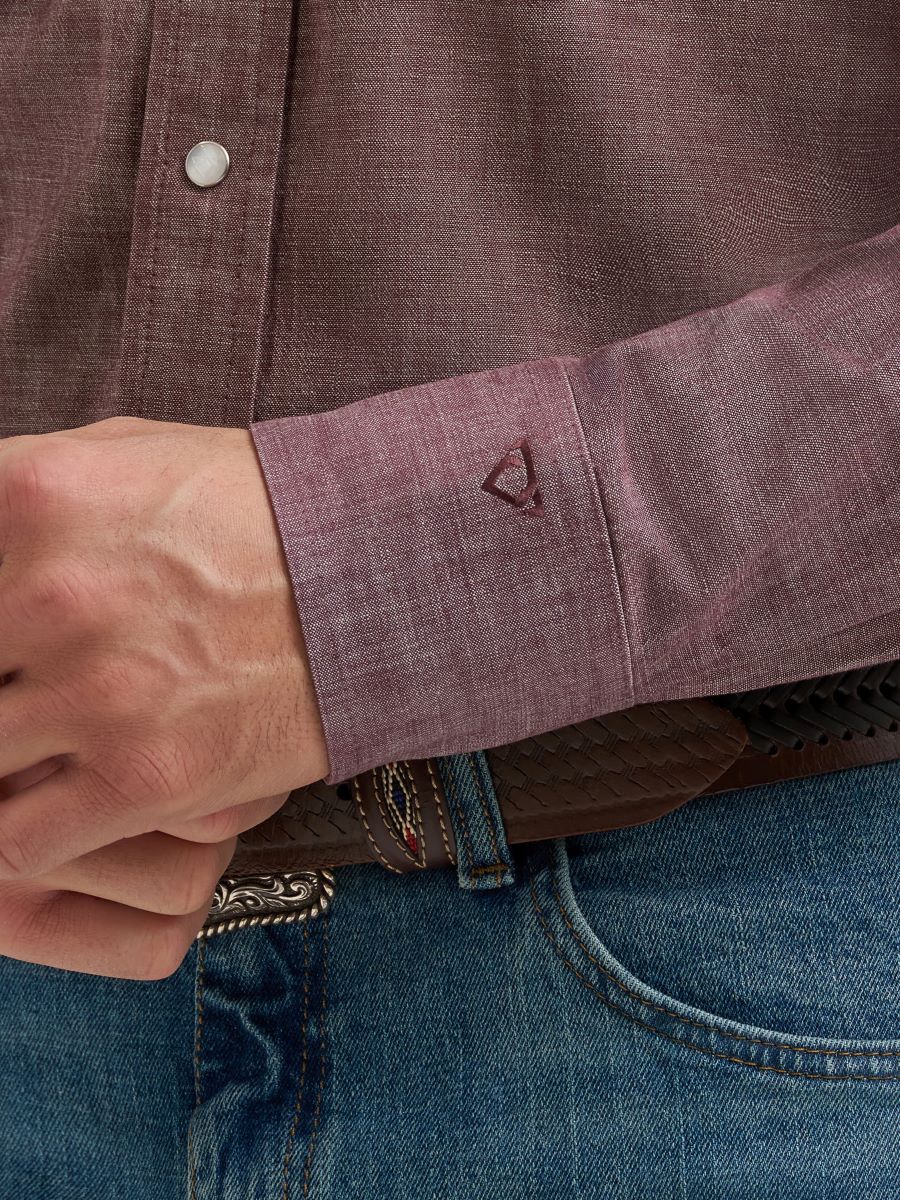 Close-up of a person wearing a brown Wrangler shirt with rolled-up sleeve and blue jeans.