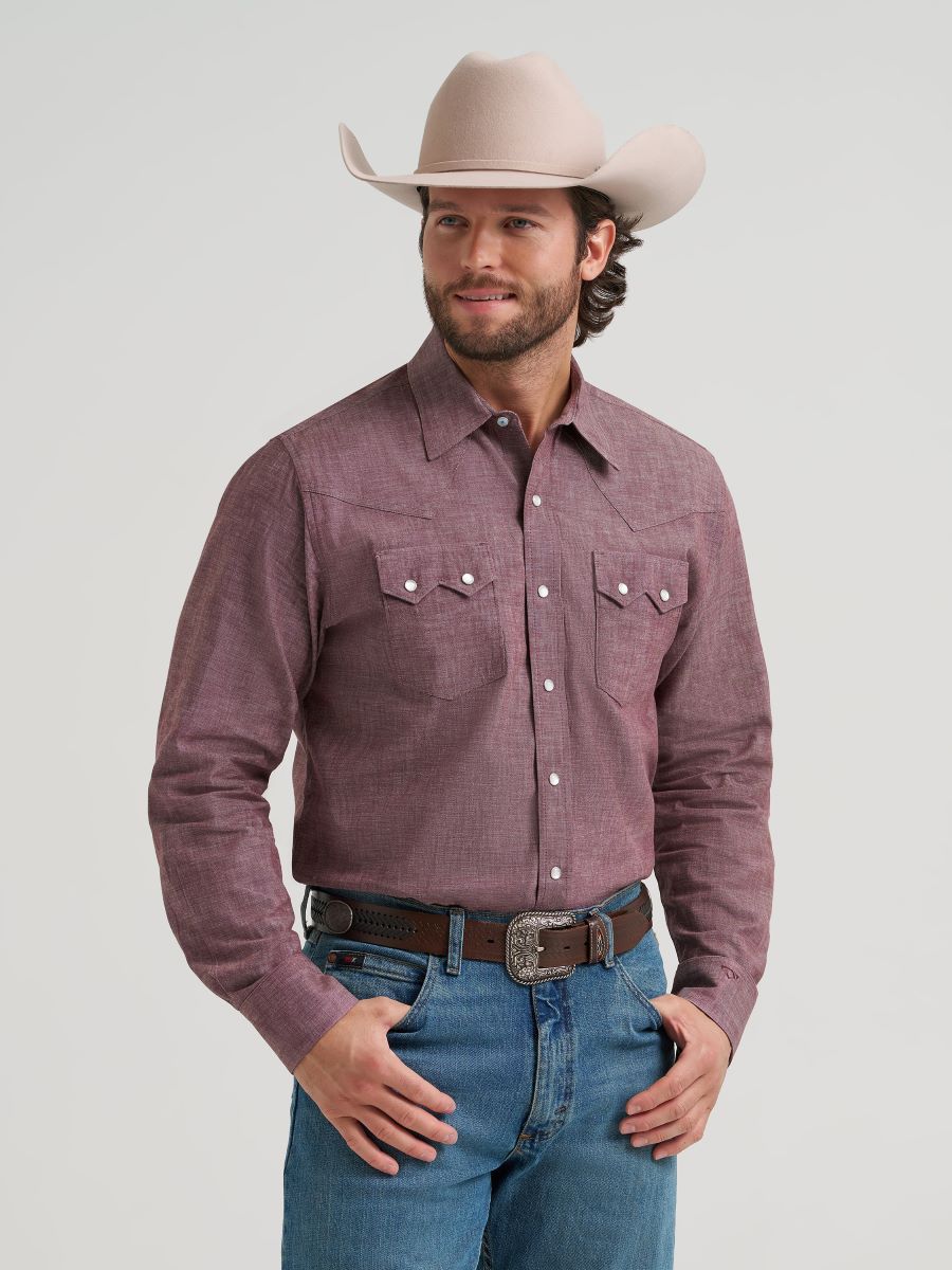 Man wearing a purple button-up Wrangler shirt, blue jeans, and a beige cowboy hat on a light gray background