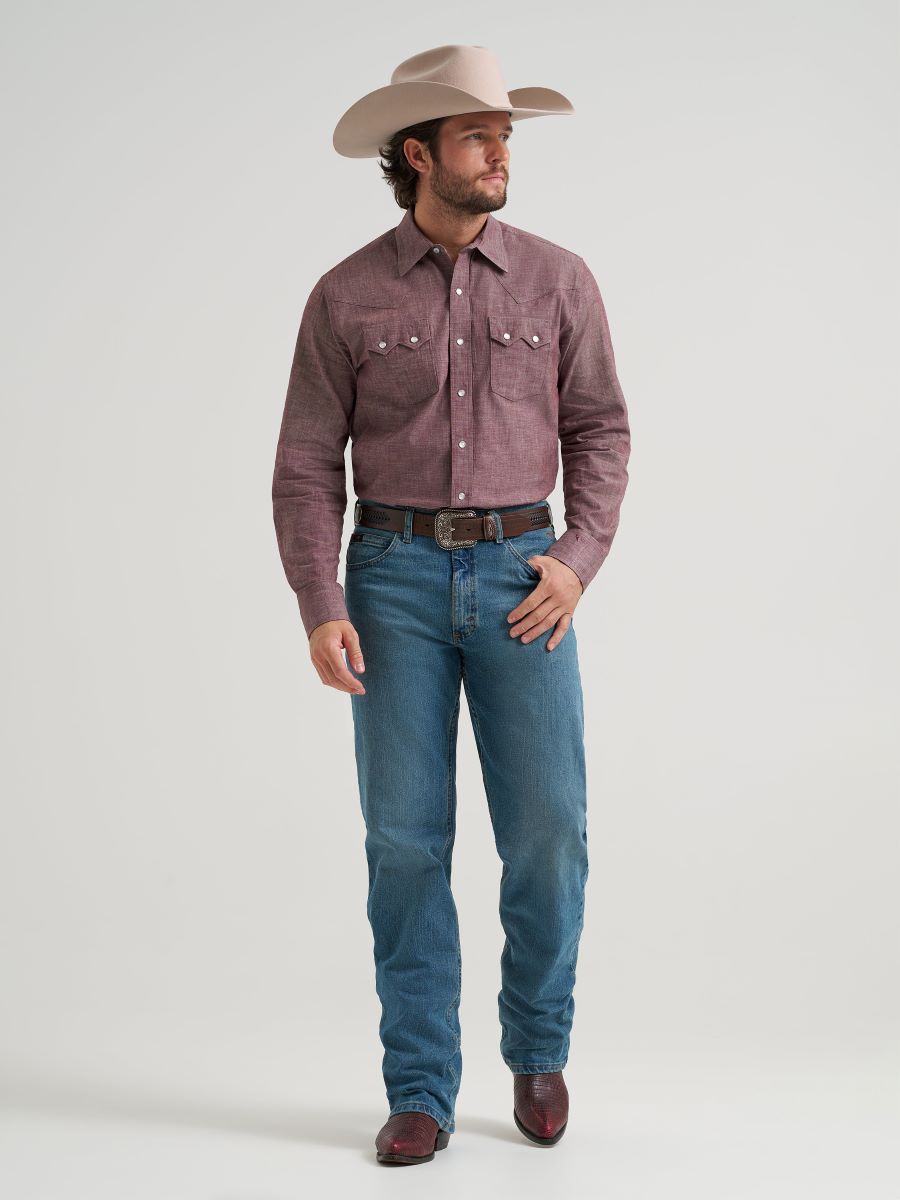 Man wearing a purple button-up Wrangler shirt, blue jeans, and a beige cowboy hat on a light gray background