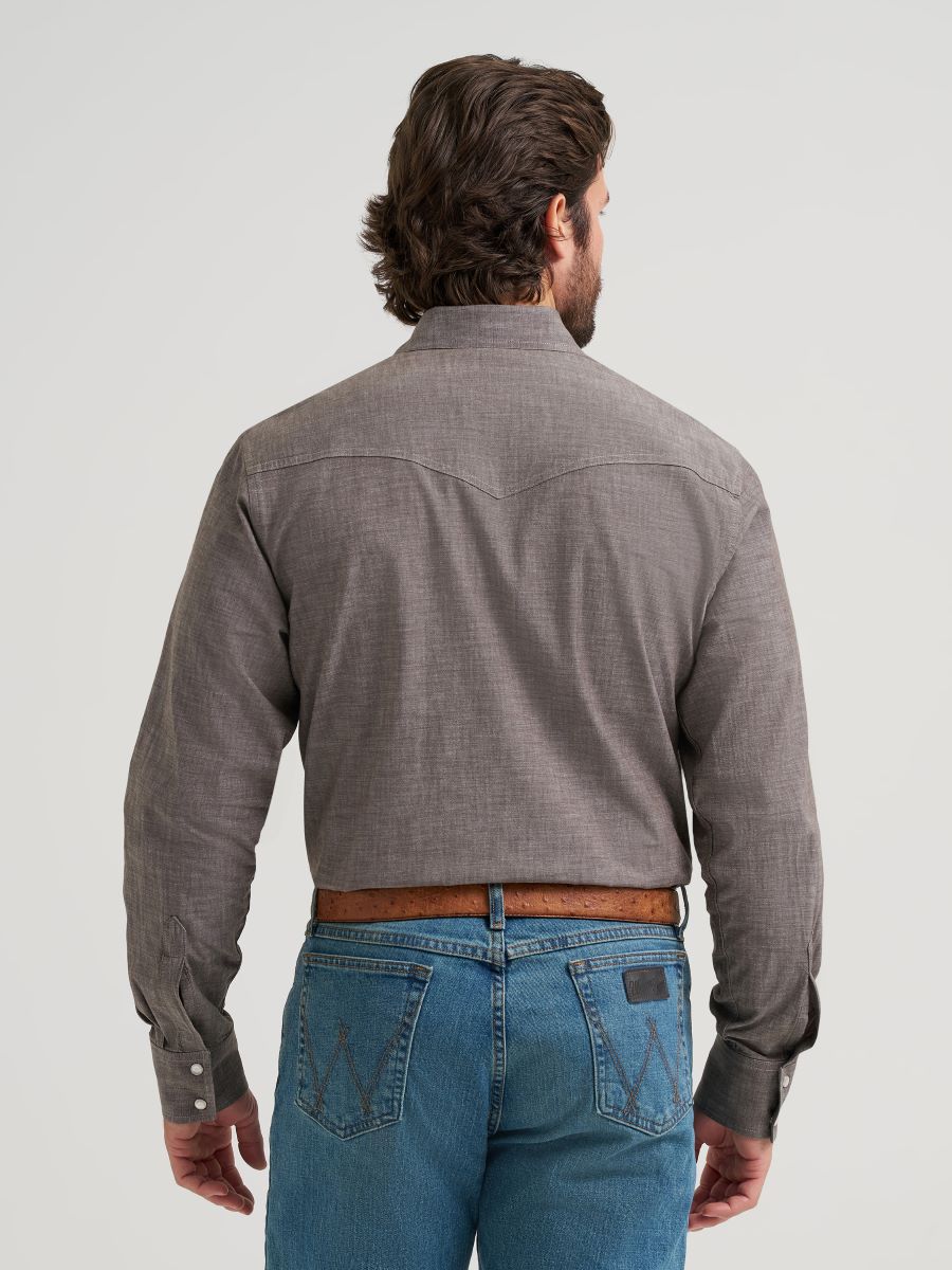 Man wearing a gray button-up Wrangler shirt and blue jeans on a light gray background