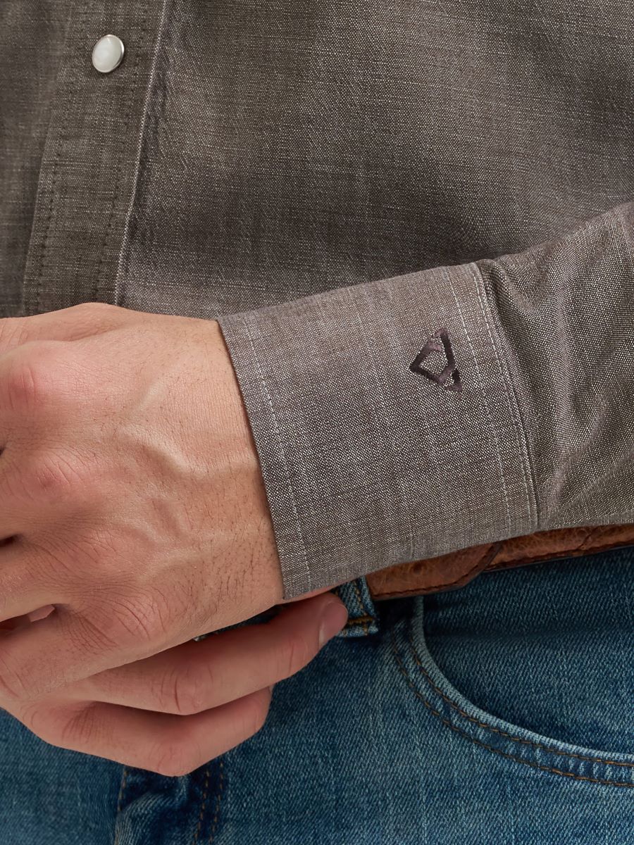 Close-up of a person wearing a gray Wrangler shirt with rolled-up sleeve and blue jeans.
