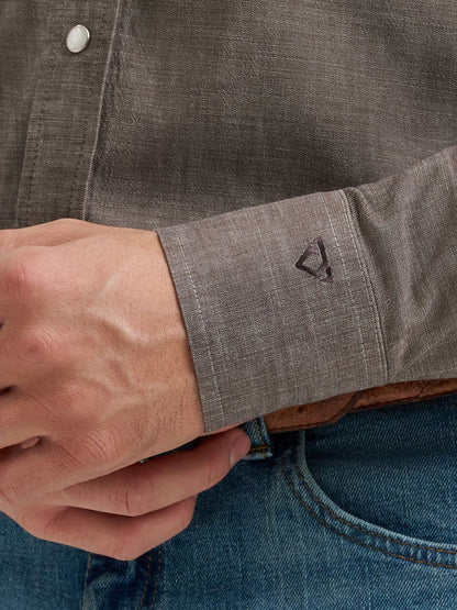 Close-up of a person wearing a gray Wrangler shirt with rolled-up sleeve and blue jeans.