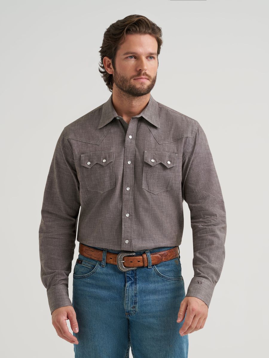 Man wearing a gray button-up Wrangler shirt and blue jeans on a light gray background