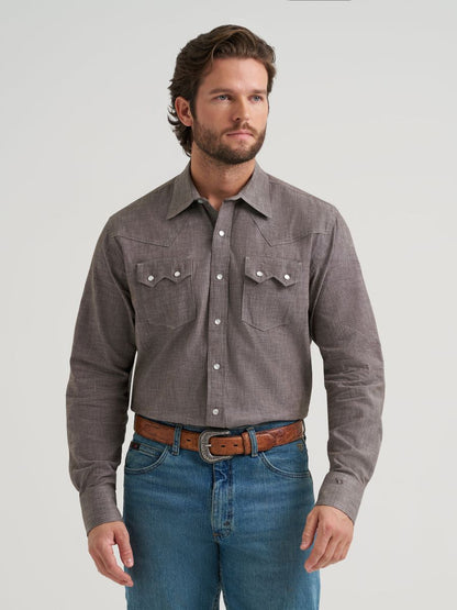 Man wearing a gray button-up Wrangler shirt and blue jeans on a light gray background