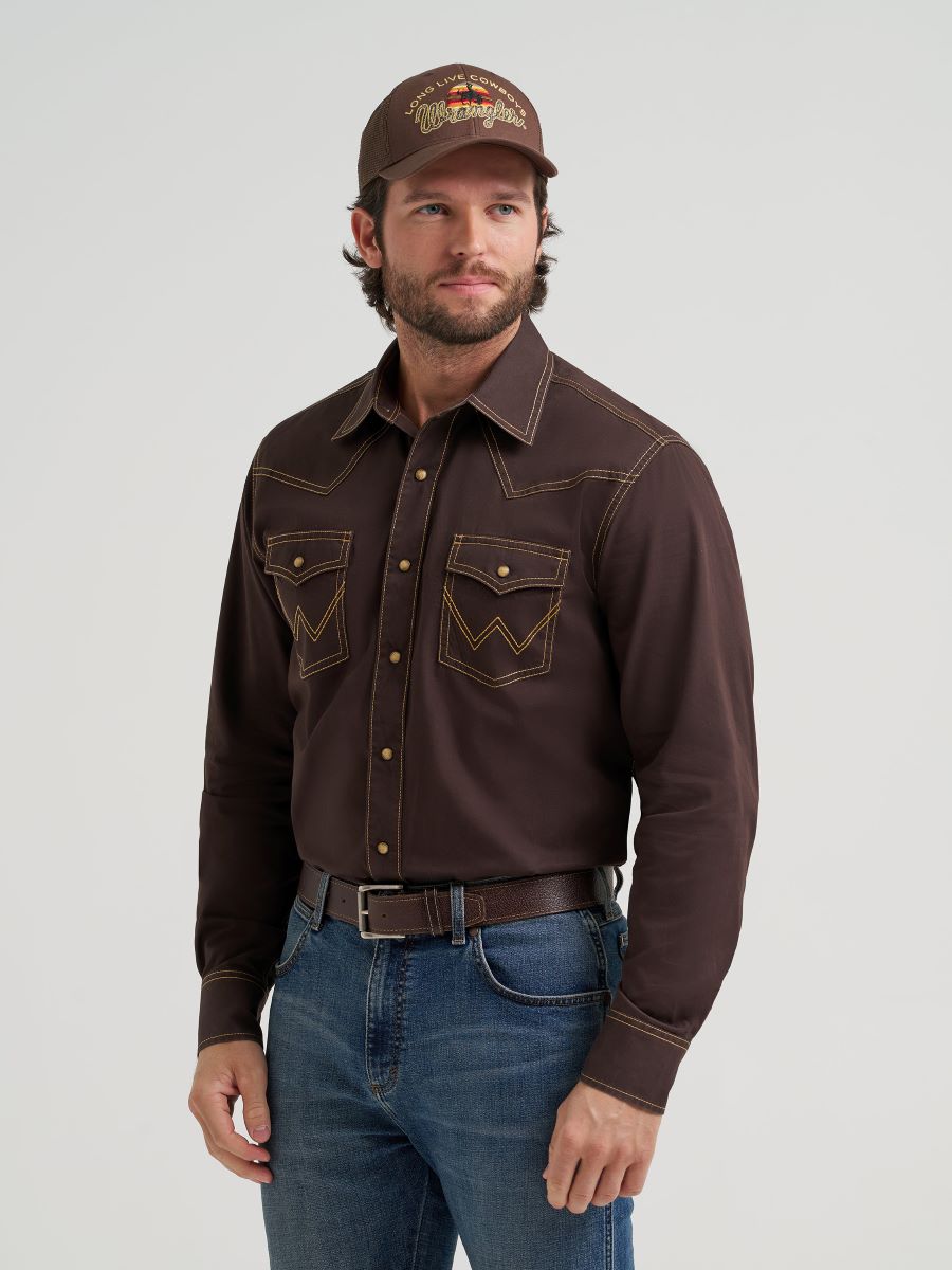 Man wearing a brown Wrangler western-style shirt, jeans, and cap on a light gray background