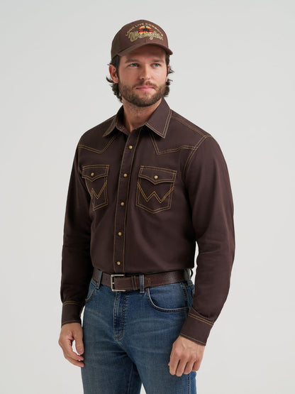 Man wearing a brown Wrangler western-style shirt, jeans, and cap on a light gray background