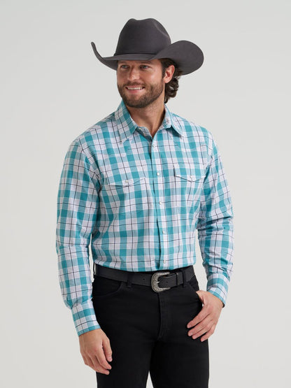 Man wearing a turquoise plaid Wrangler shirt, black pants, and a cowboy hat on a light gray background