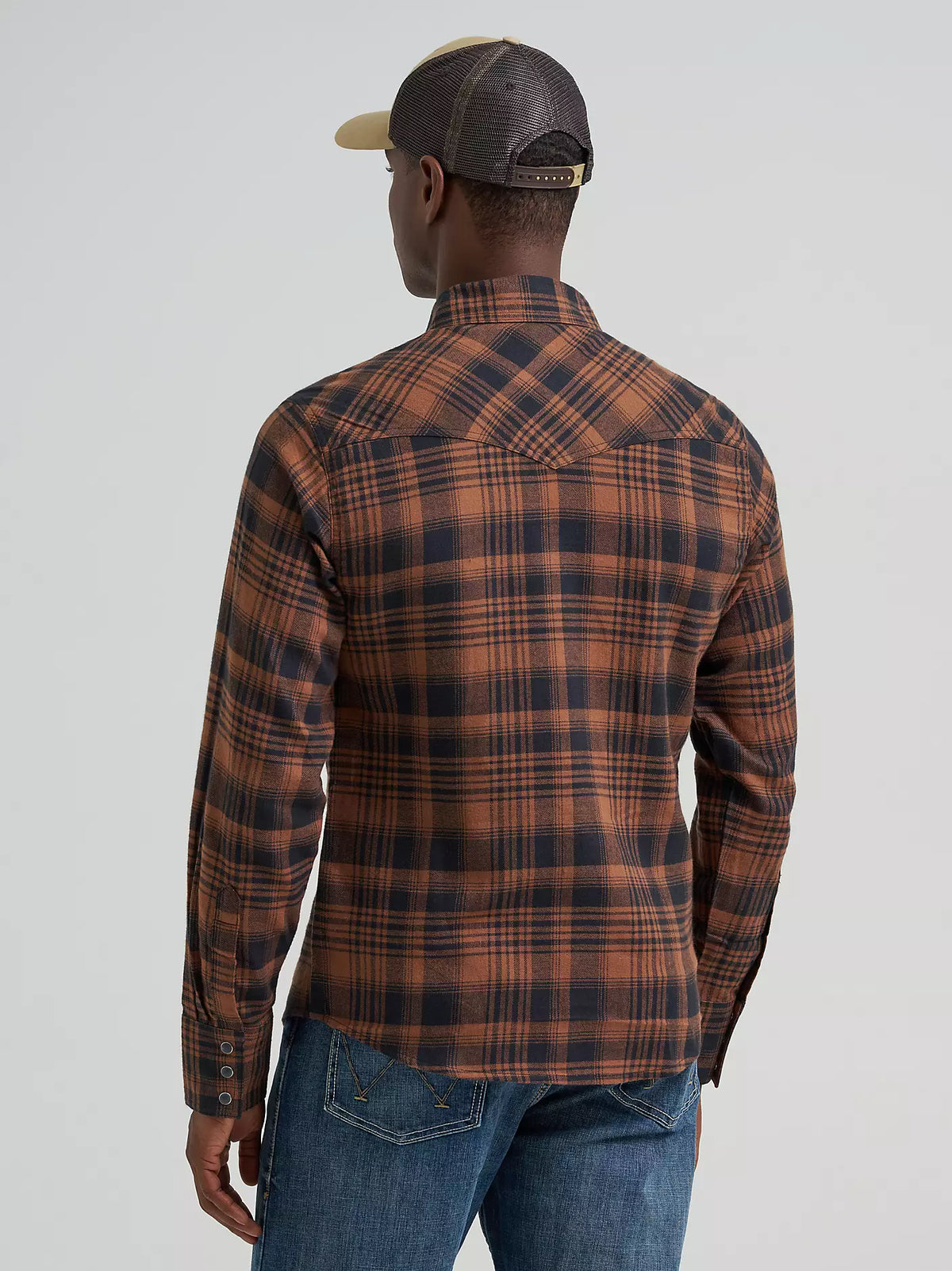 man wearing a brown plaid Wrangler flannel shirt, blue jeans and a ball cap on a grey background