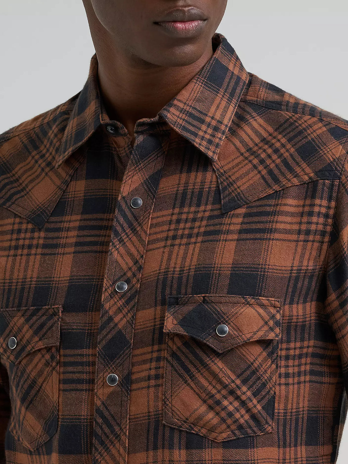 close up of a man wearing a brown flannel from Wrangler on a grey background