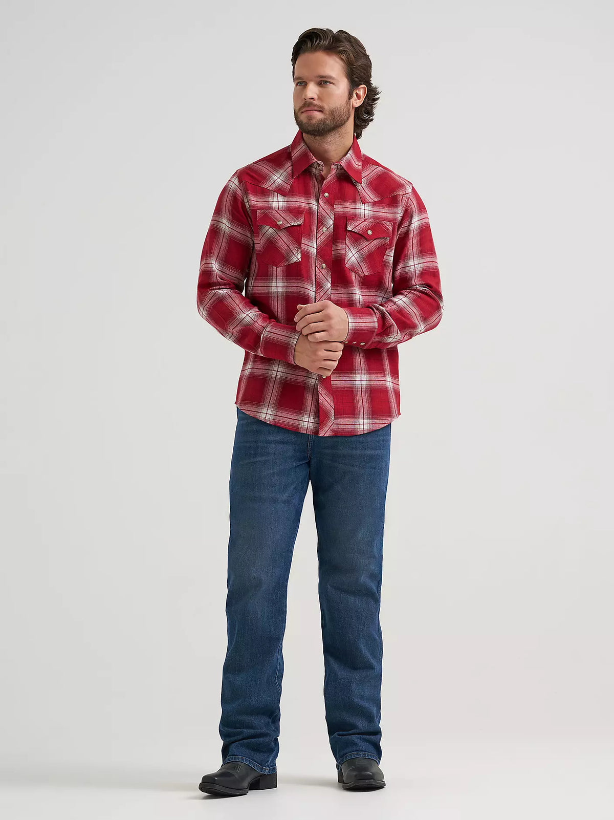 man wearing a red plaid flannel by Wrangler and blue jeans on a grey background