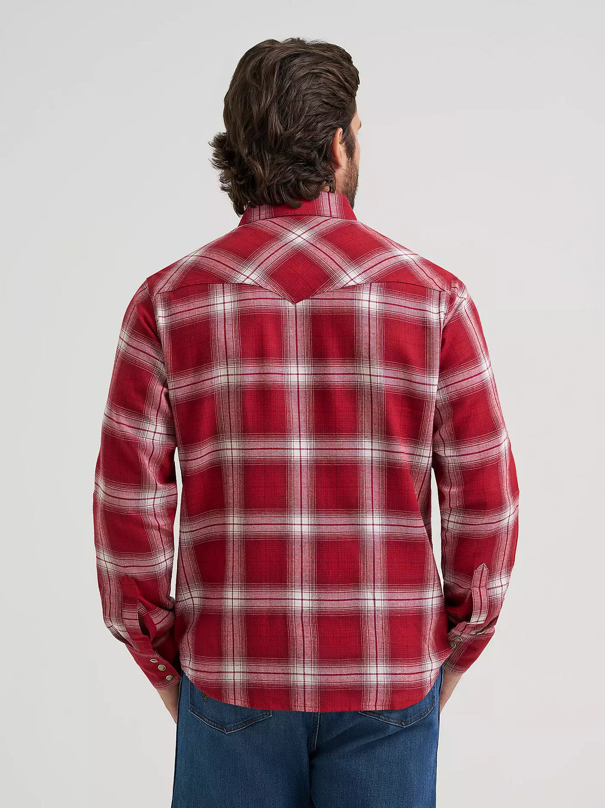 man wearing a red plaid flannel by Wrangler and blue jeans on a grey background
