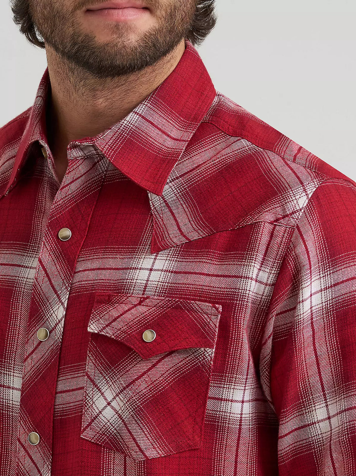 close up of a man wearing a red plaid flannel y Wrangler on a grey background