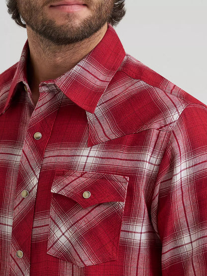 close up of a man wearing a red plaid flannel y Wrangler on a grey background