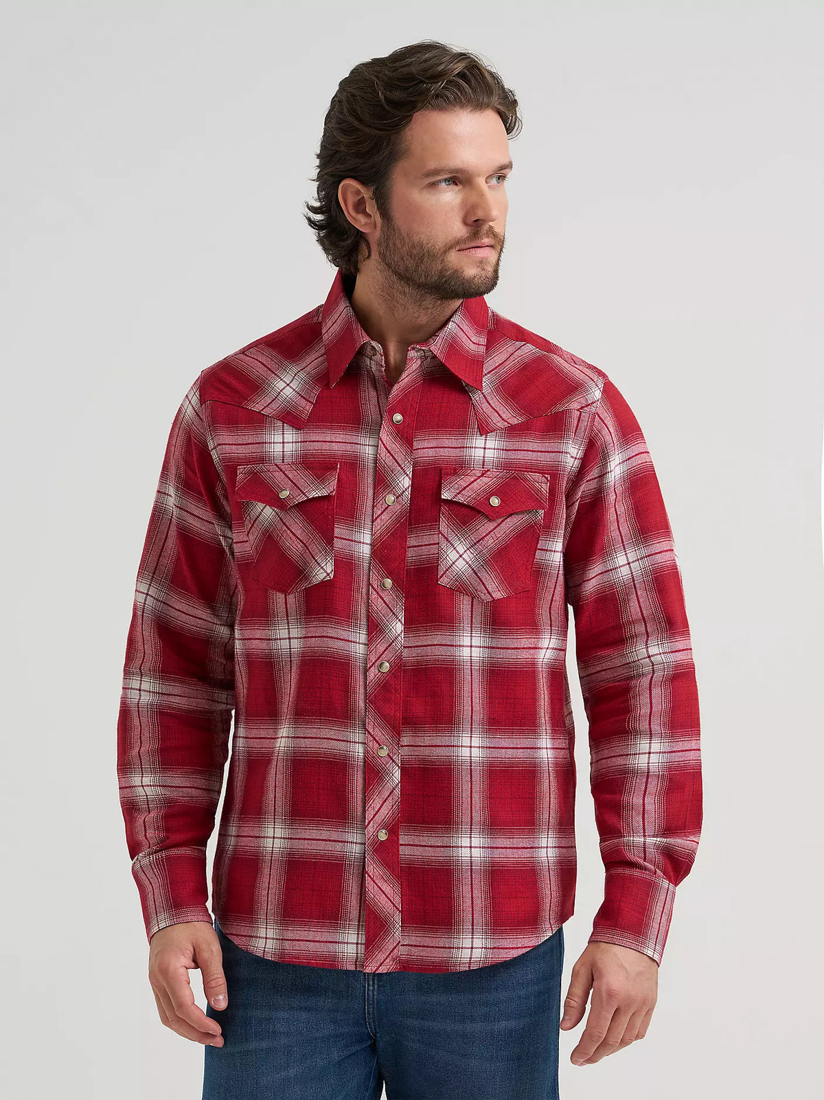 man wearing a red plaid flannel by Wrangler and blue jeans on a grey background