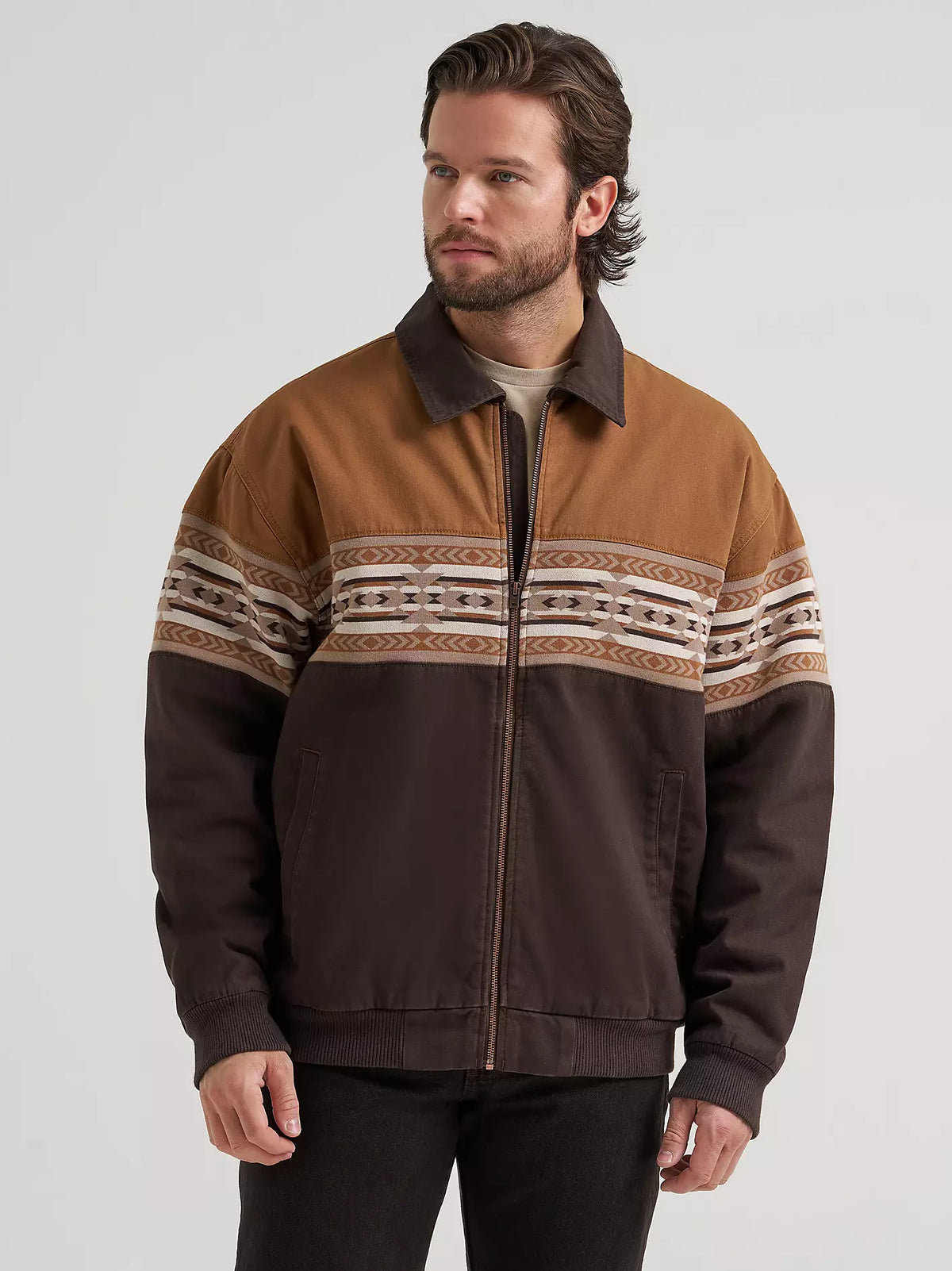 Man wearing a brown Wrangler bomber jacket and black jeans on a white background