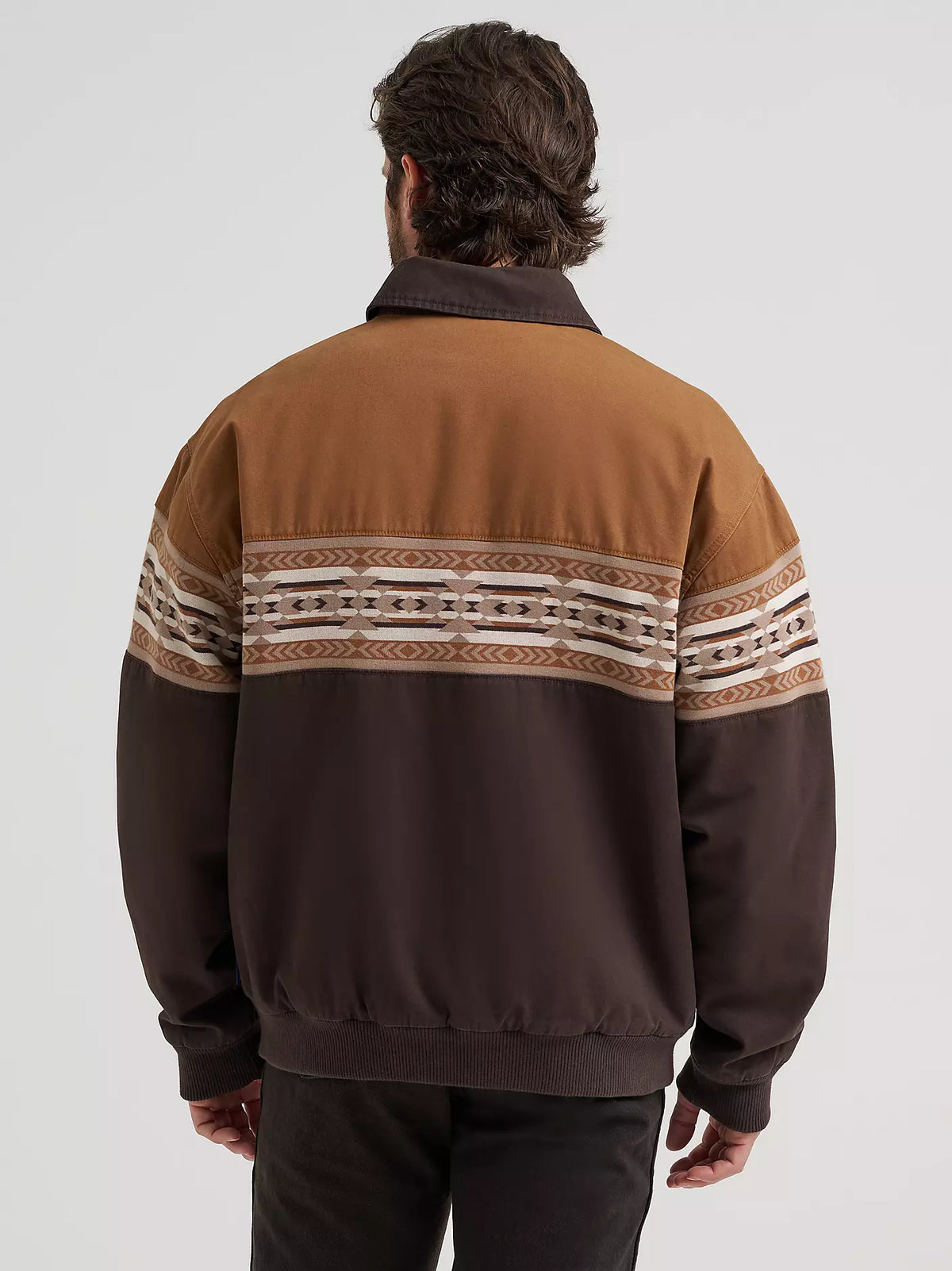 Man wearing a brown Wrangler bomber jacket and black jeans on a white background