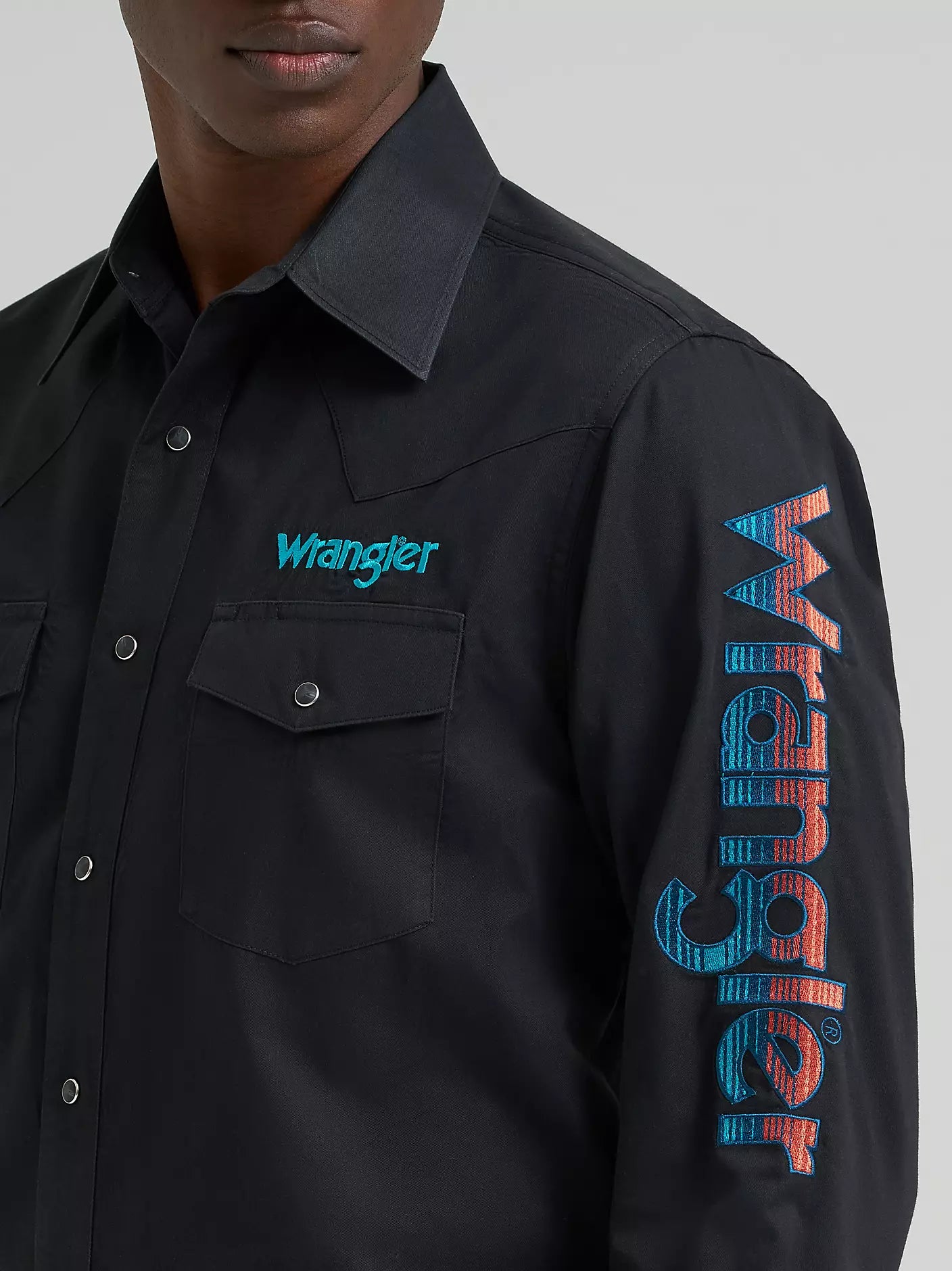 Person wearing a black Wrangler shirt with branding on a gray background