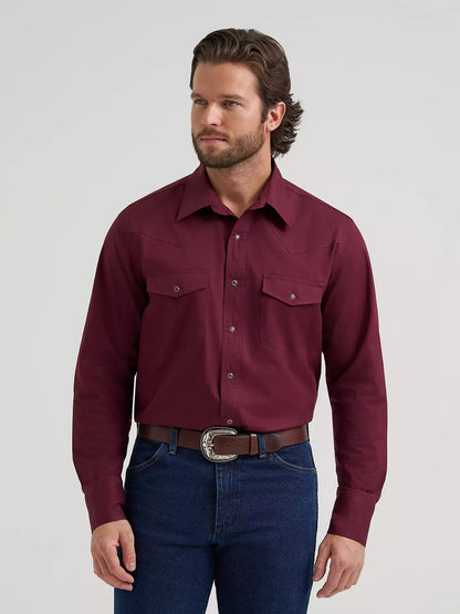 A man wearing a long-sleeve Wrangler button-down shirt in deep burgundy, paired with dark blue jeans and a brown belt with a silver buckle, photographed against a light gray studio background.