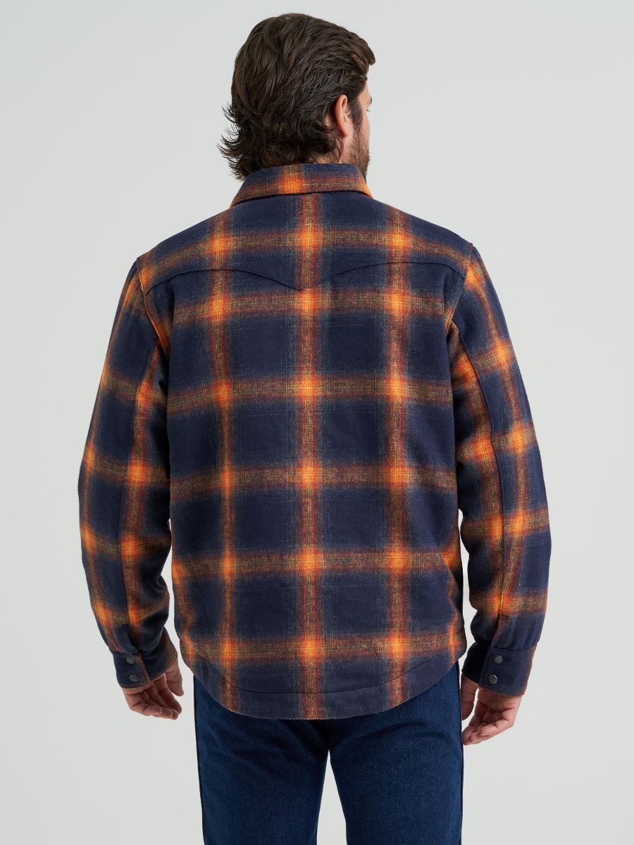 Man wearing a blue and orange Wrangler flannel jacket and blue jeans on a grey background