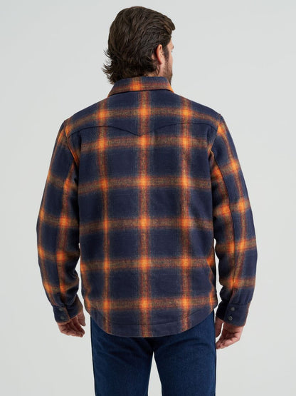 Man wearing a blue and orange Wrangler flannel jacket and blue jeans on a grey background