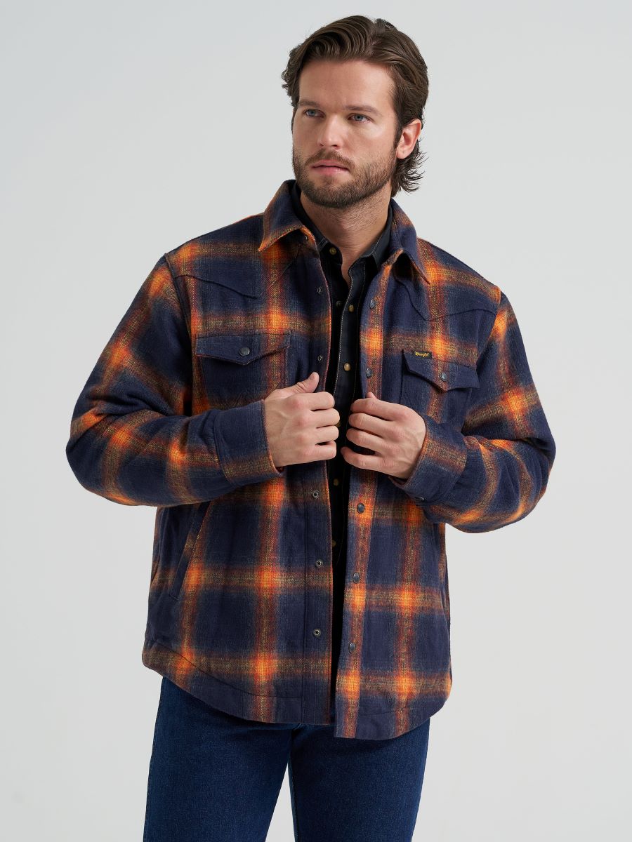 Man wearing a blue and orange Wrangler flannel jacket and blue jeans on a grey background